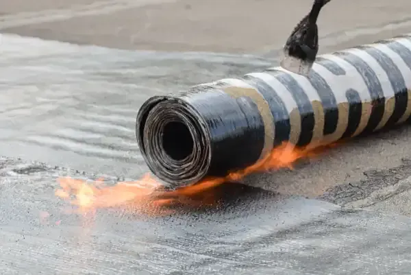 A person is rolling a roll of roofing material on a roof.
