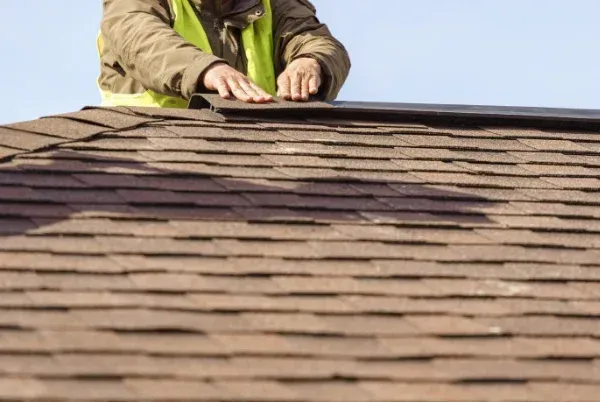 A man in a yellow vest is working on a roof.
