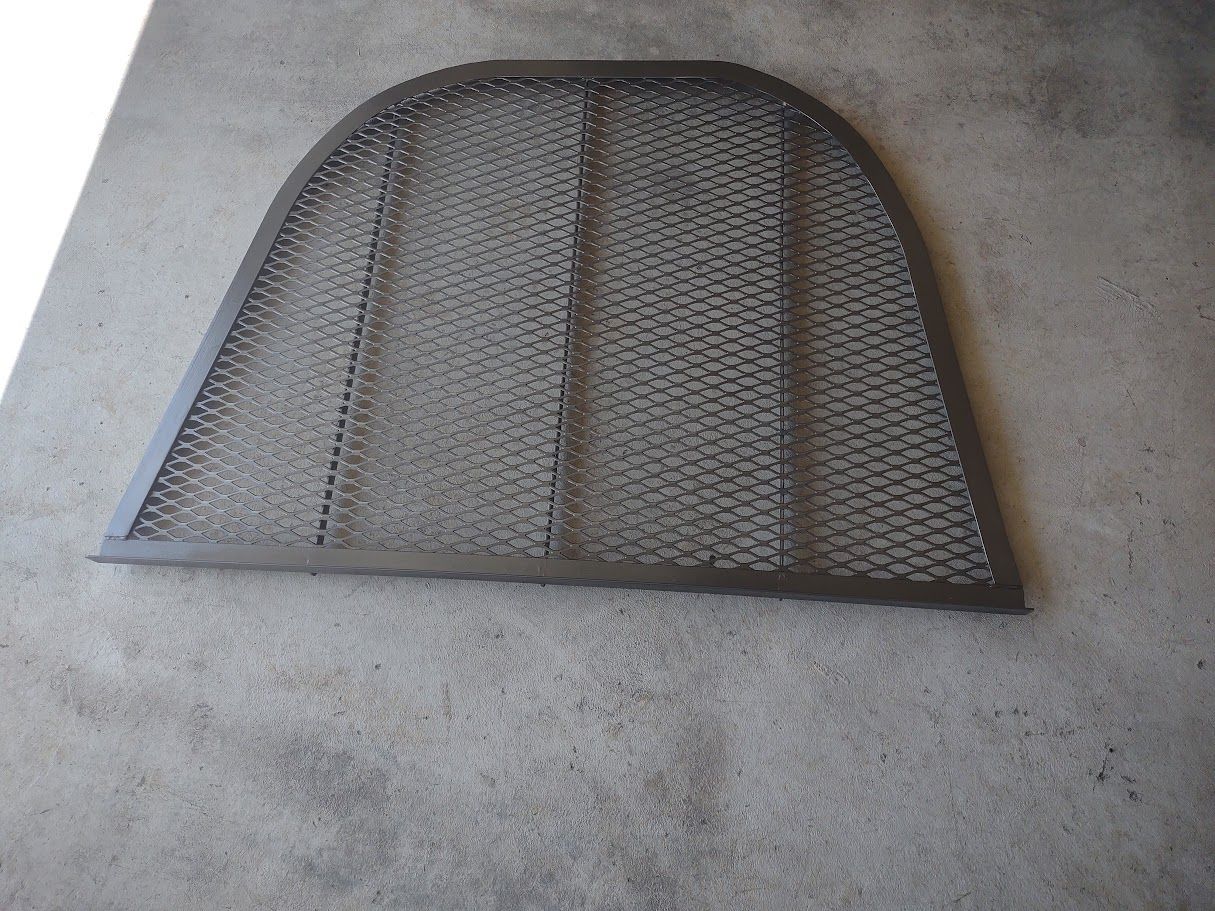 A metal, arched-top grate or screen with a honeycomb mesh design lying on a concrete floor.