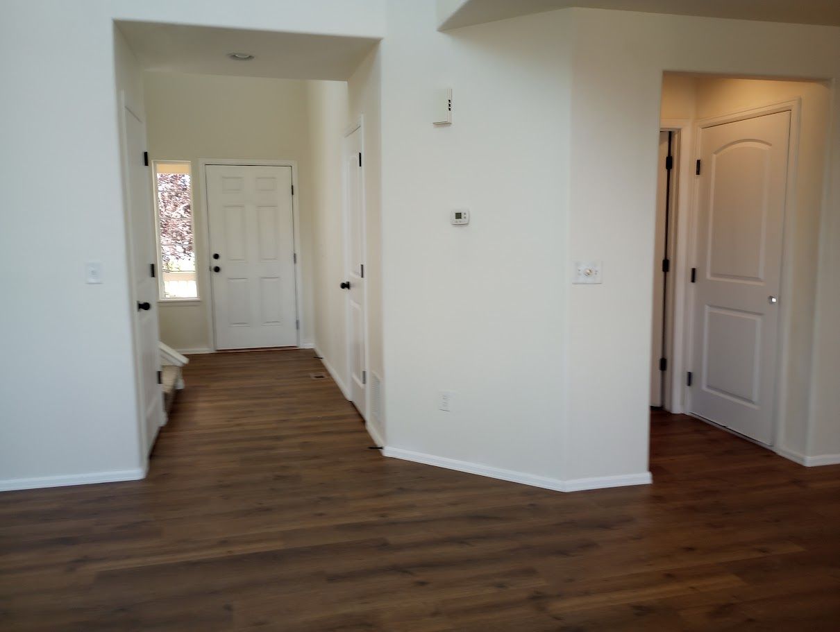 Interior view of an entryway with light-colored walls, wood-look flooring, and multiple white interior doors.
