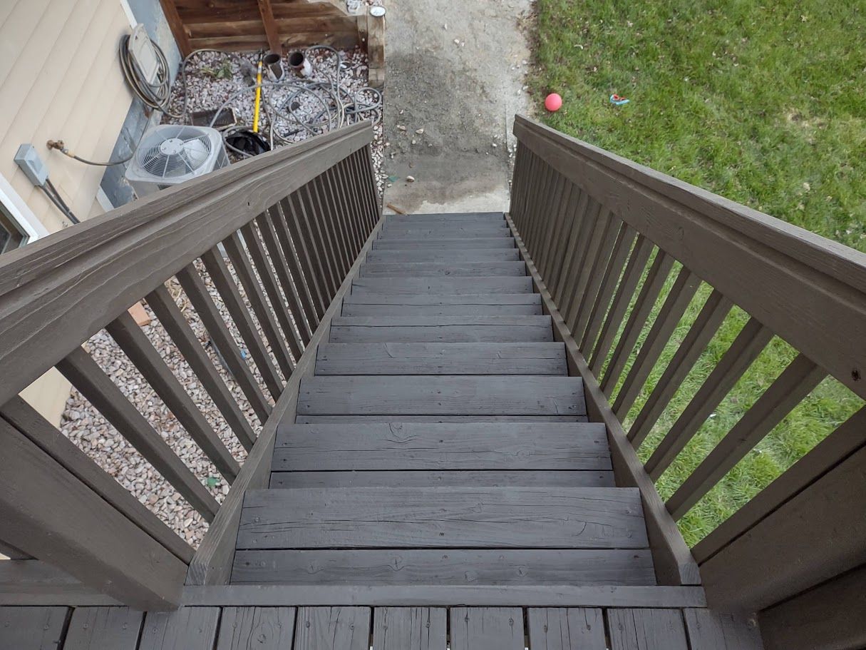 High-angle view of gray wooden stairs leading down to a gravel path and grassy yard.