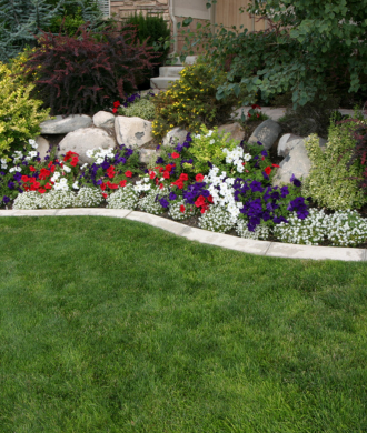 Curved flower bed with red, white, and purple blooms beside a green lawn and stone border