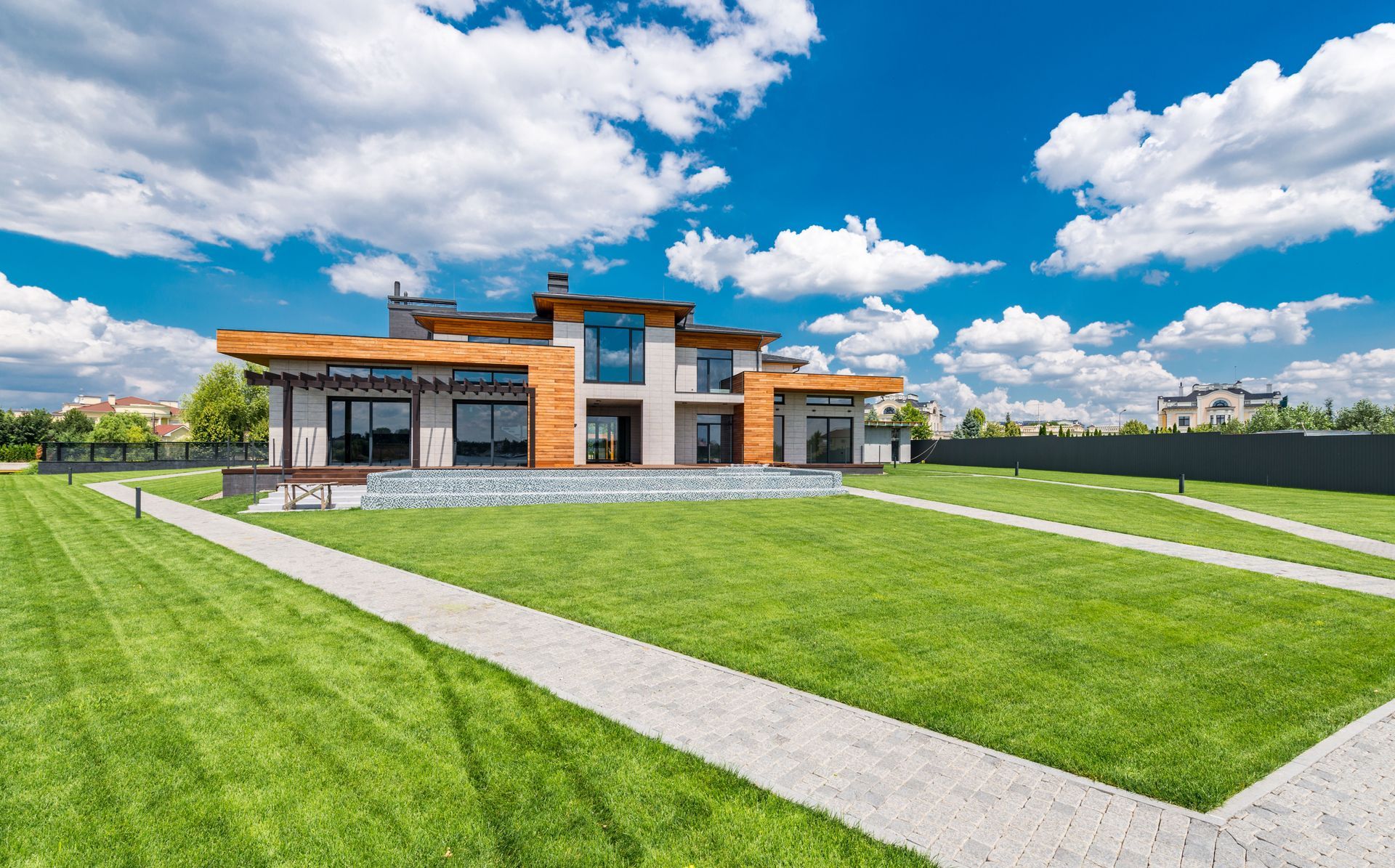 Modern brick building with large windows beside a wide green lawn under a bright blue sky with clouds