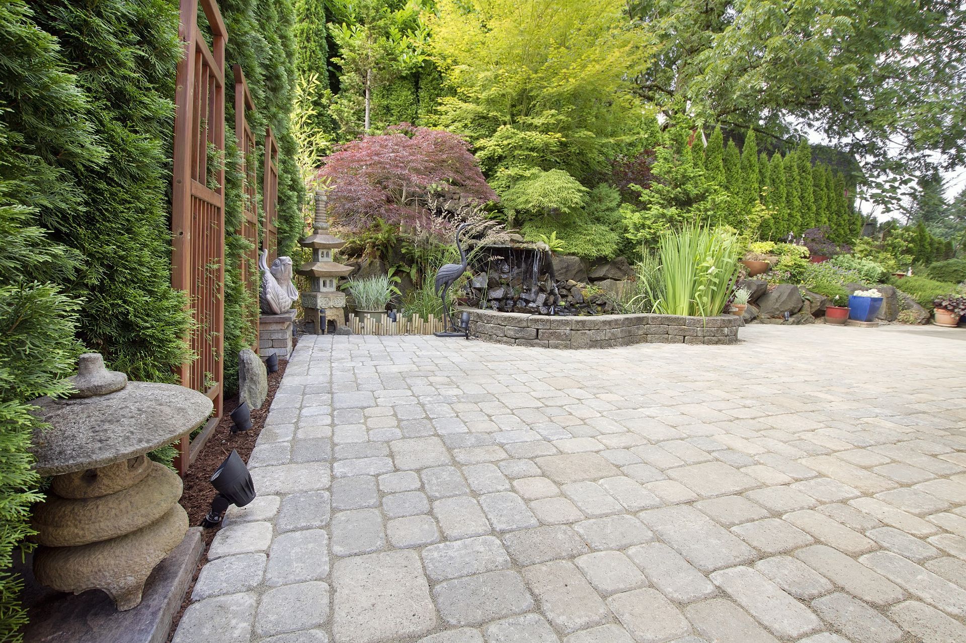 Stone patio beside a garden wall with potted plants, trees, and a small waterfall feature