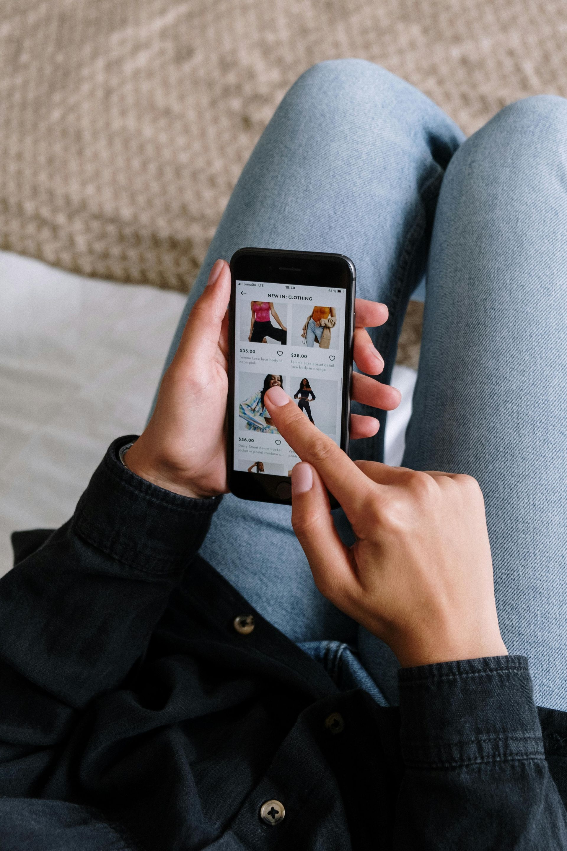 Hands using a smartphone on a couch, browsing a clothing shopping app.