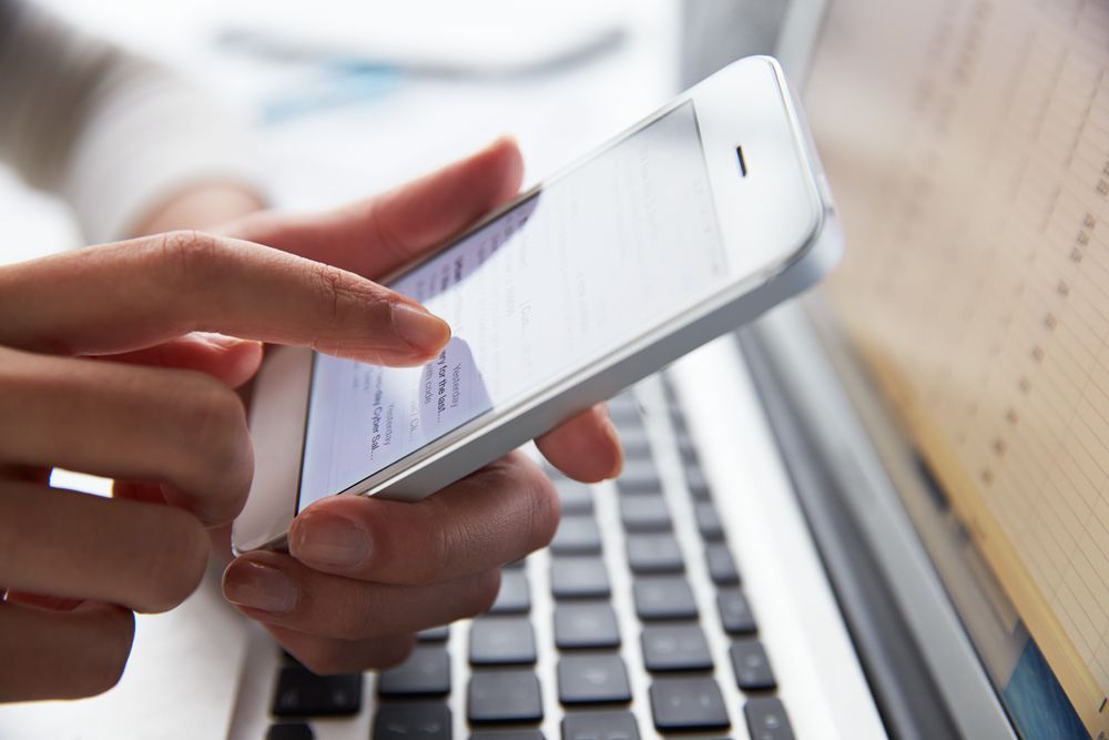 person at laptop using mobile phone
