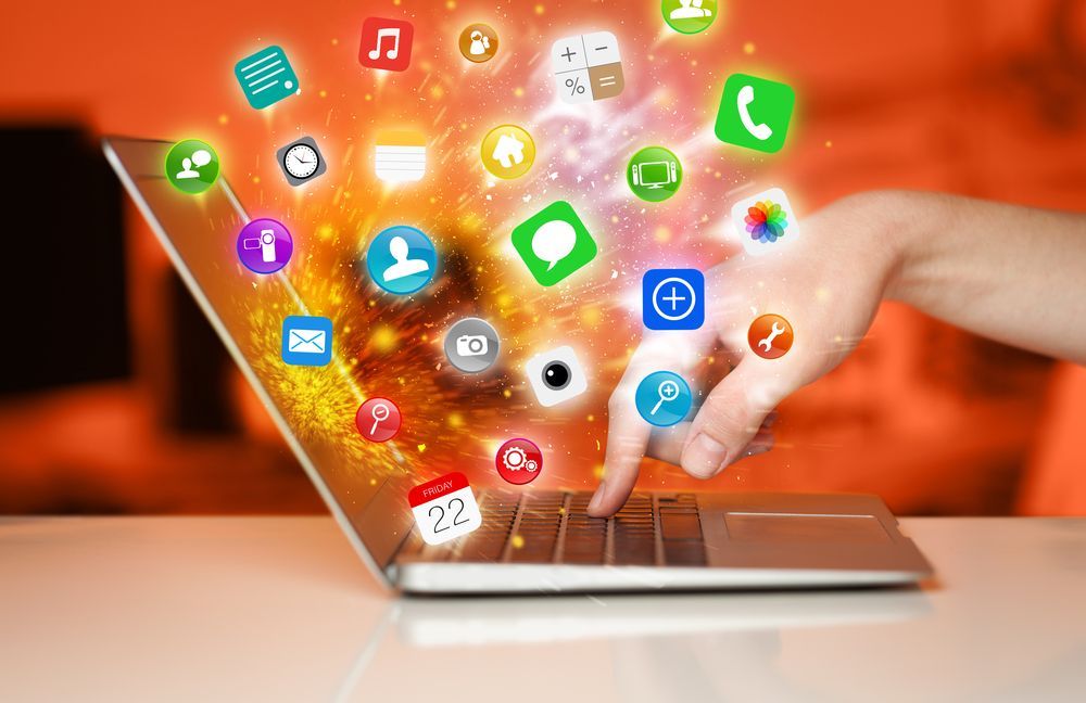 A person types on a laptop, with a vibrant, colorful explosion of various app icons emerging from the screen.