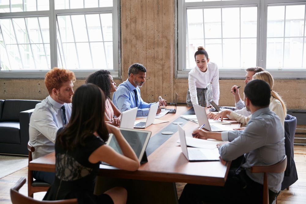 People in a meeting around a table with laptops and papers in a bright office