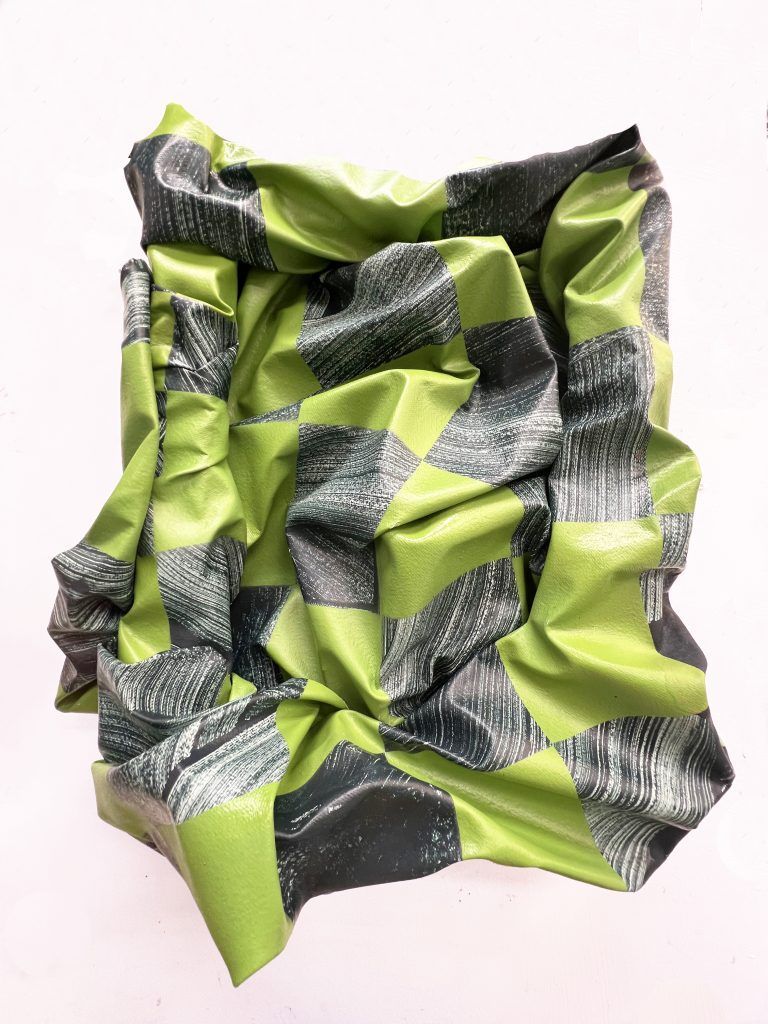 A crumpled sheet with a repeating pattern of bright lime green and textured dark grey geometric shapes.