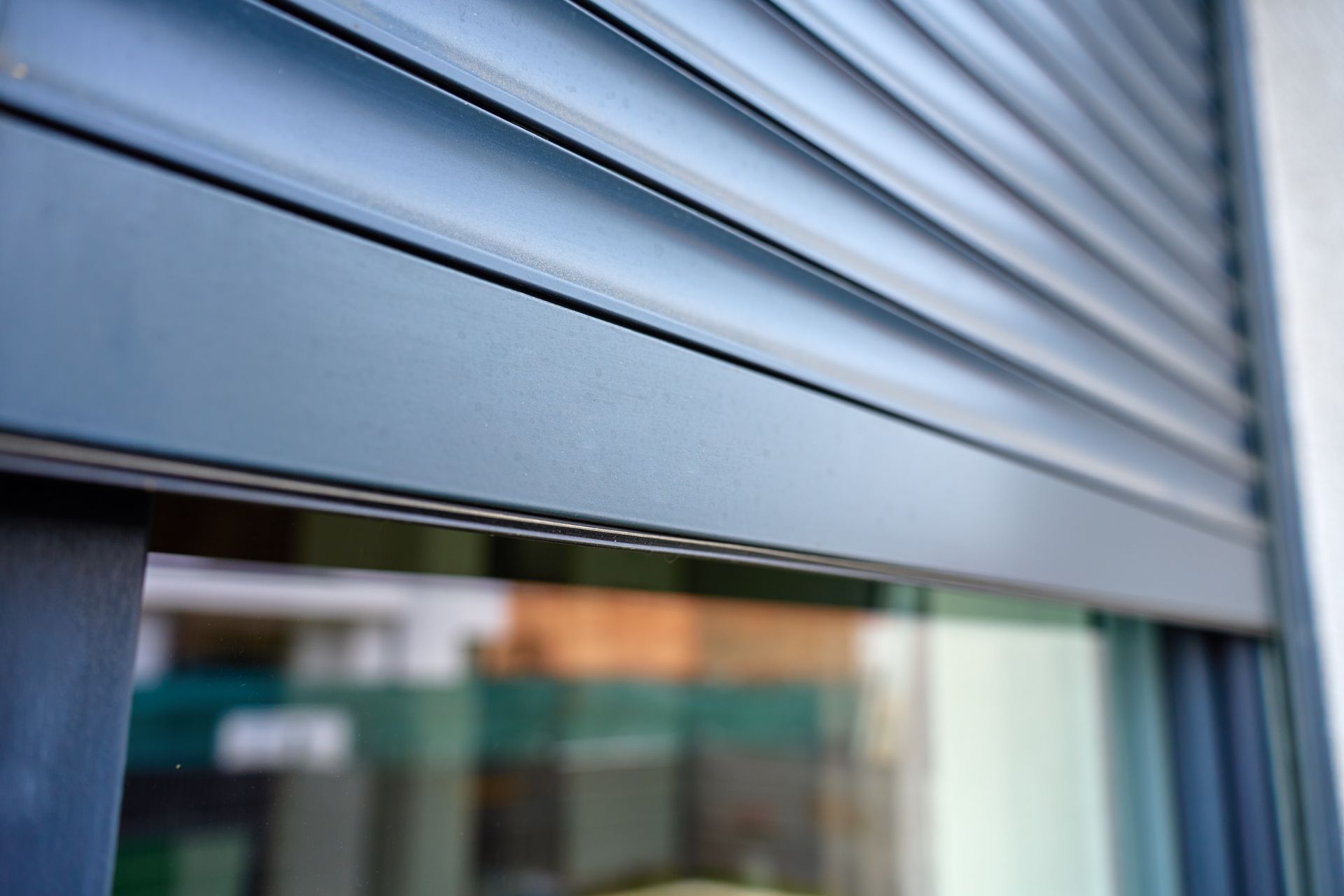 A close-up of a modern metal roller shutter partially covering a window on a building exterior. A close-up of a modern metal roller shutter partially covering a window on a building exterior.