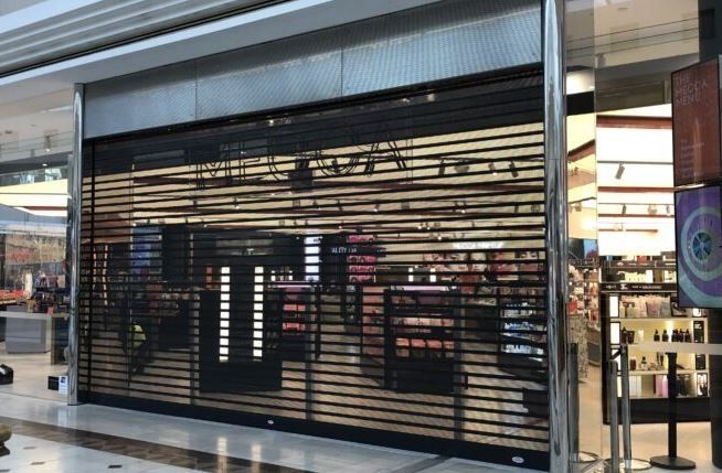 A closed storefront in a shopping mall with a black metal security gate lowered over the entrance.