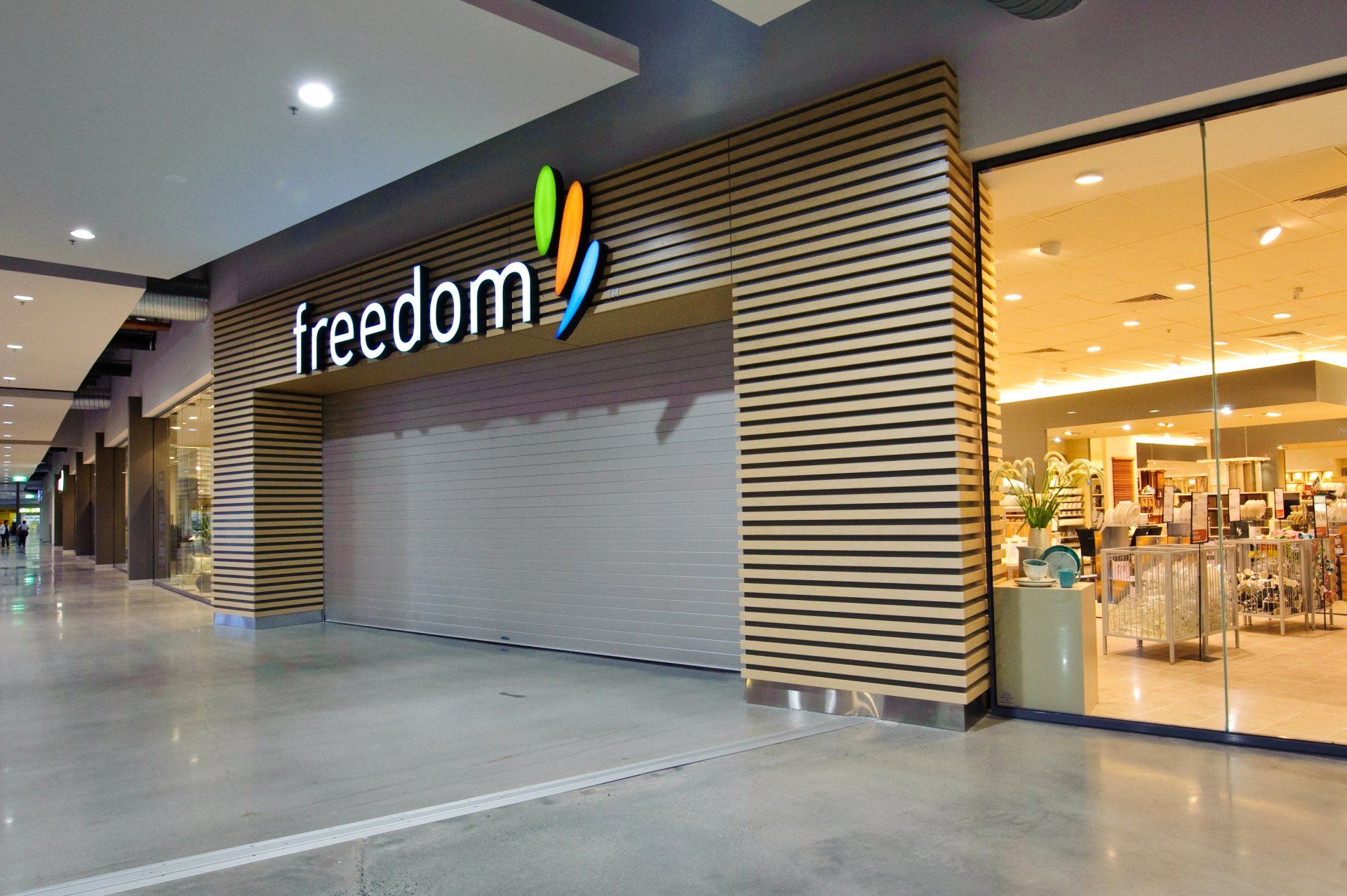 The Freedom furniture store storefront in a shopping mall, featuring a wood-paneled entrance with a closed metal shutter.