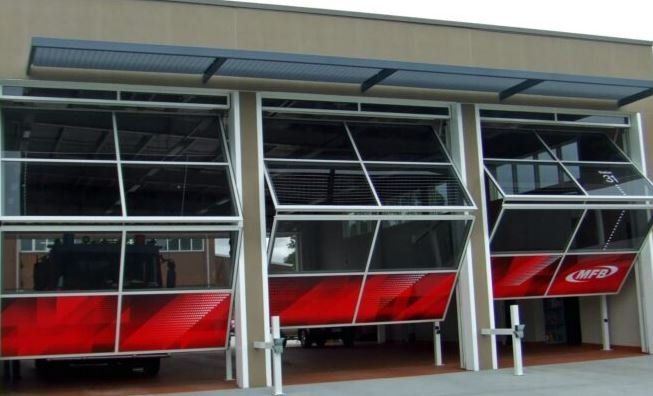 Three fire station bays with large, modern glass doors folded open to reveal a fire truck inside.