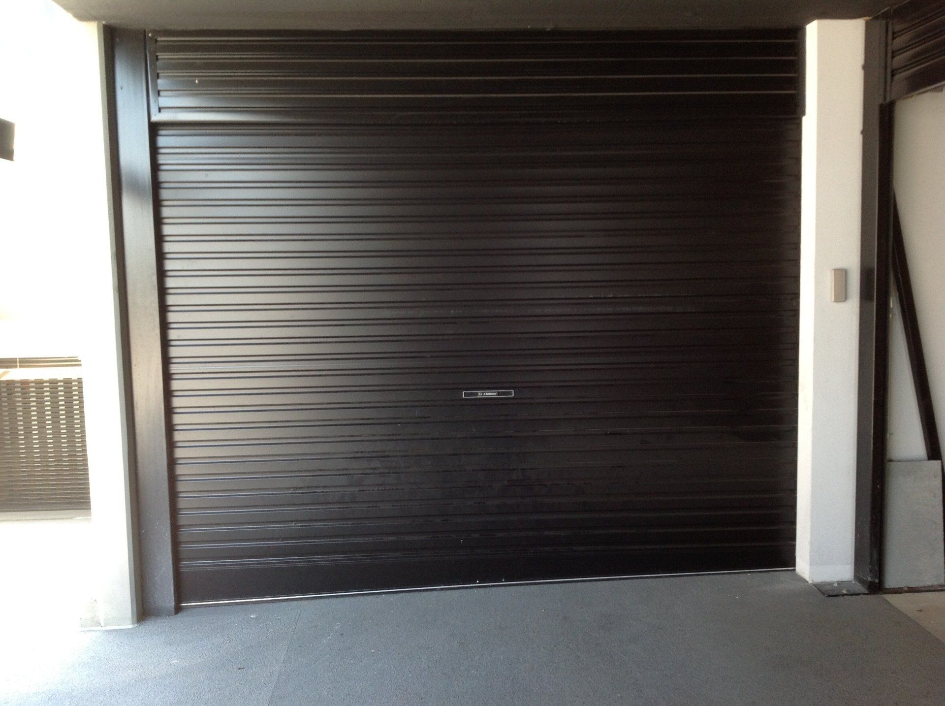 A closed dark brown horizontal-slatted metal roller garage door in a covered parking space.
