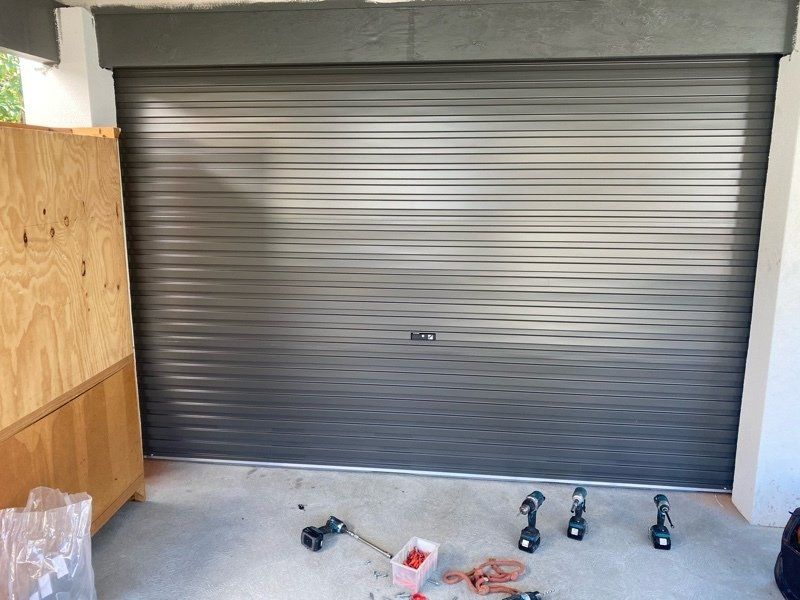 A gray roll-up garage door with tools scattered on the concrete floor in front of it.