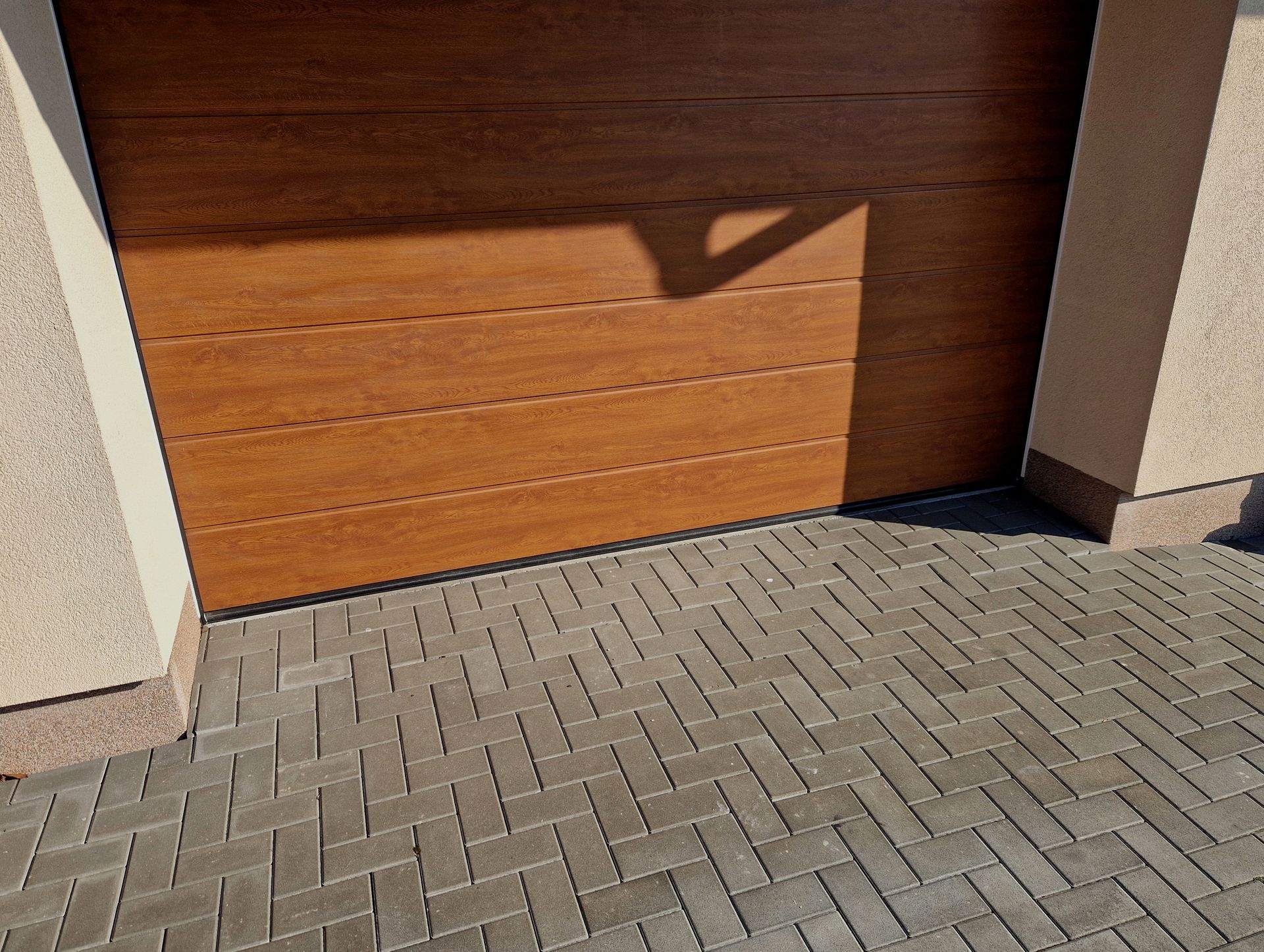 Wooden garage door with shadow on brick driveway.