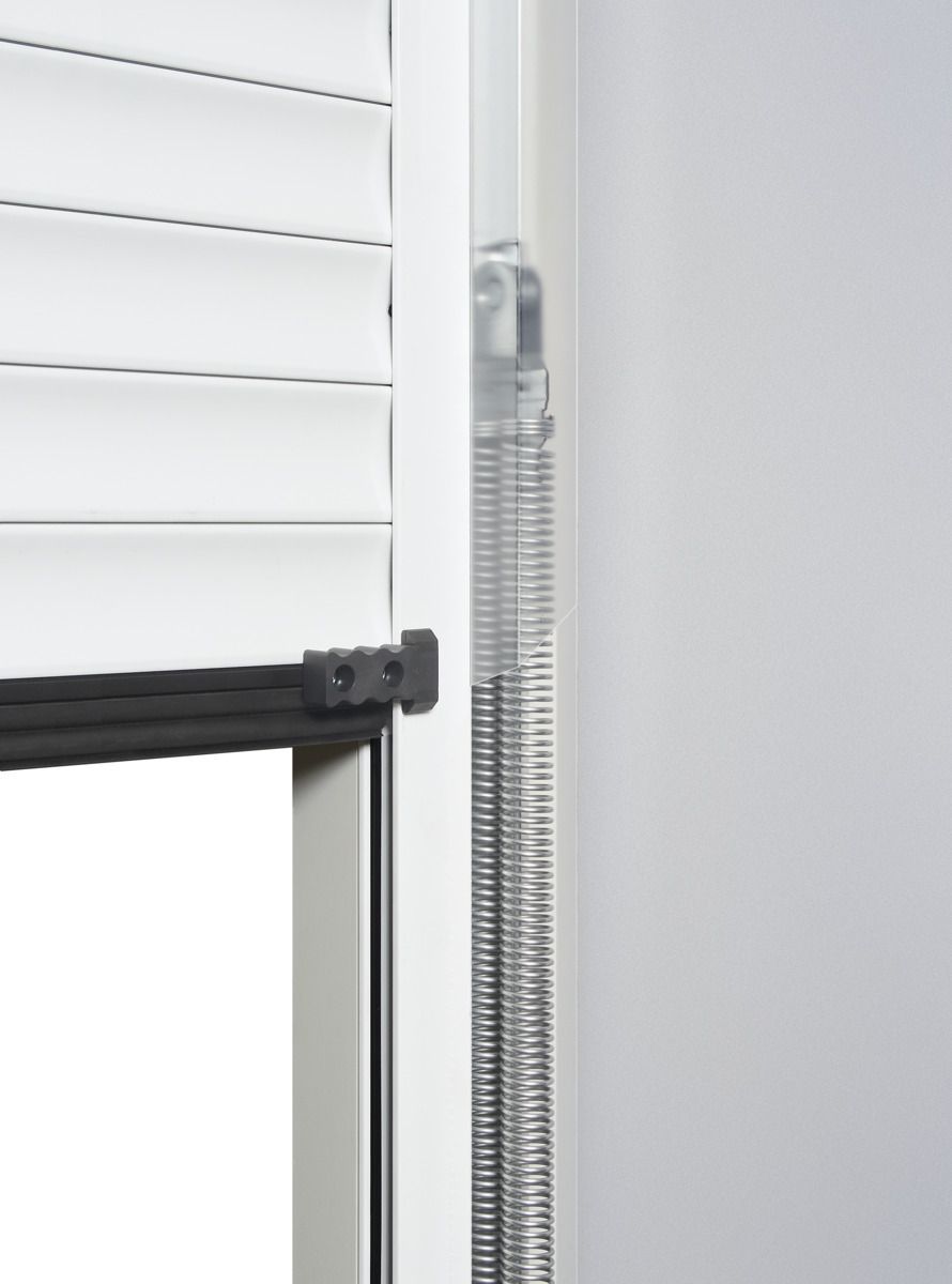 A side-view close-up of a white window blind with a clear, coiled tension spring visible in the side track.