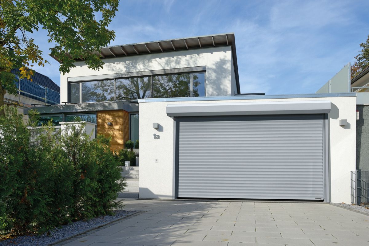 Modern white house with a gray roller garage door and a driveway under a blue sky.