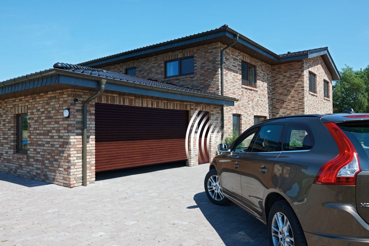 A brown SUV parked on a paved driveway in front of a brick house featuring a dark wood-paneled garage door.