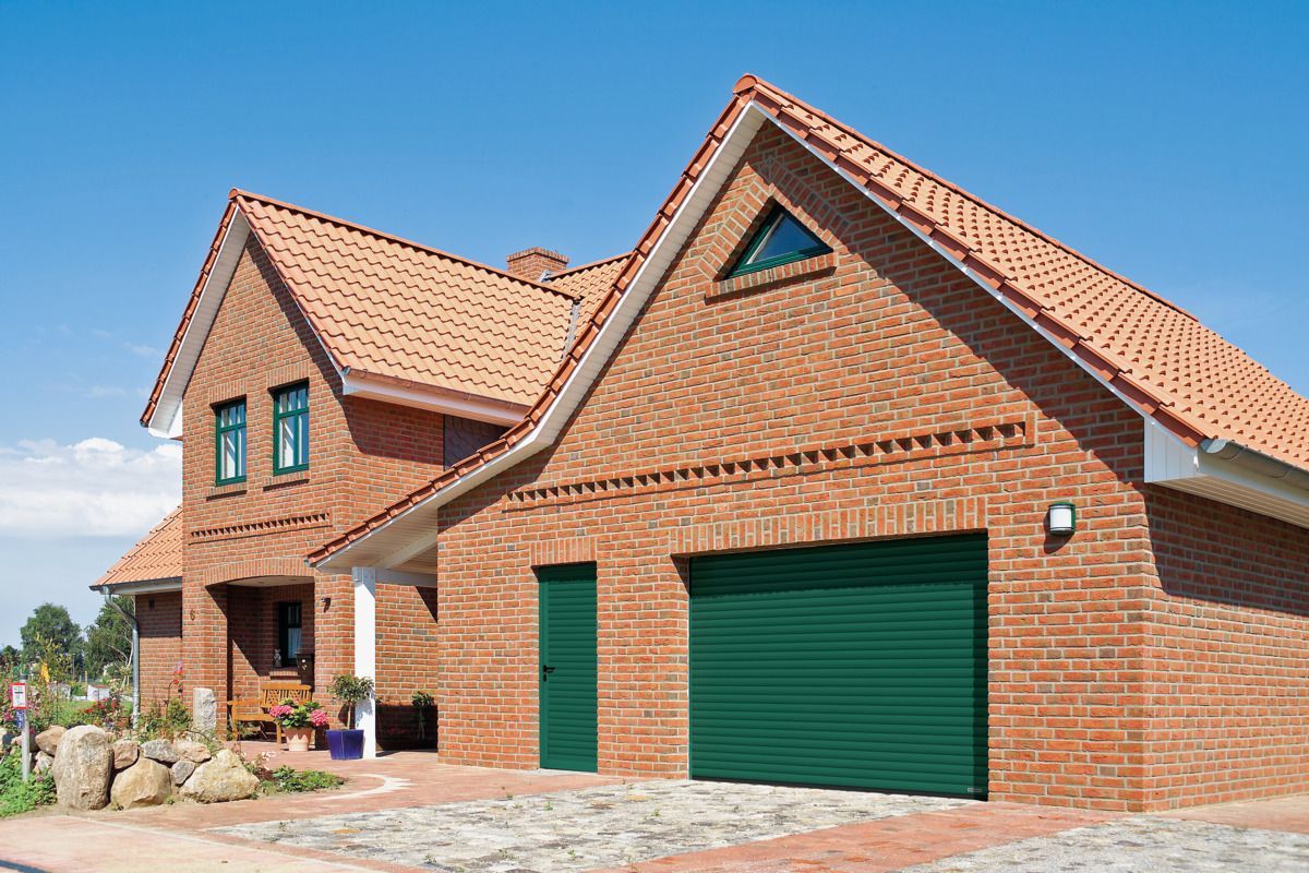 A modern red brick house with a green garage door and a matching green side door under a sunny blue sky.