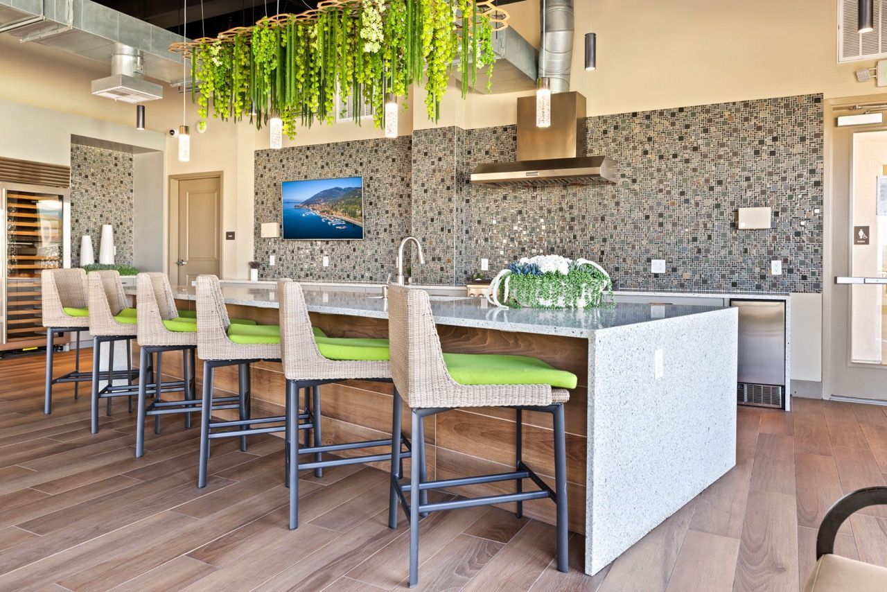 Modern community kitchen with a large island, wicker stools with green cushions, and a mosaic backsplash at Fusion Apartments in Irvine CA.