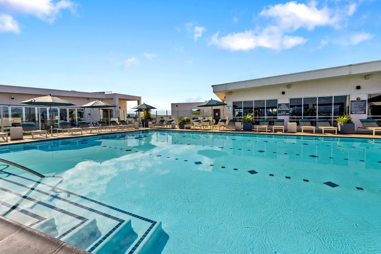 Outdoor apartment community pool with lounge chairs and umbrellas at Fusion Apartments in Irvine CA.