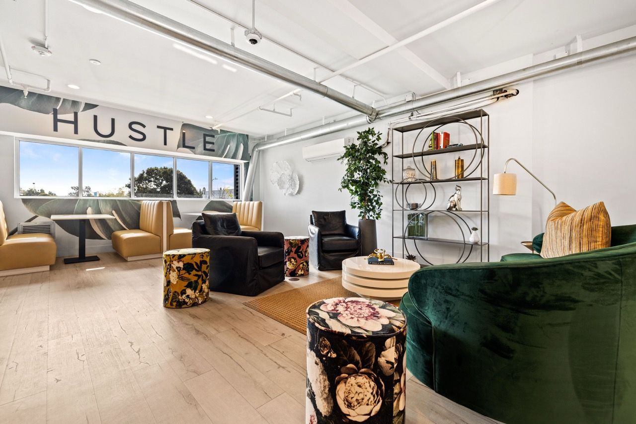 Modern communal lounge with beige seating, black chairs, and a metal shelving unit at Fusion Apartments in Irvine CA.