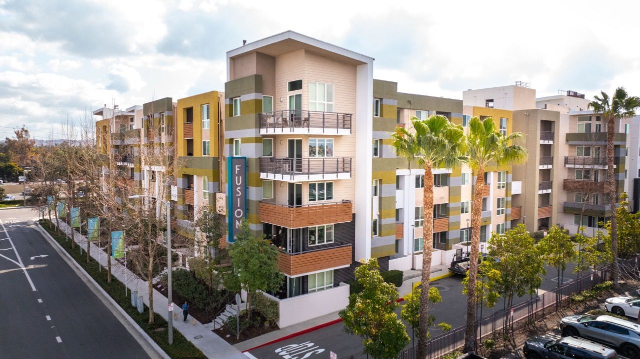 Exterior view of a modern multi-story apartment complex with colorful panels and palm trees at Fusion Apartments in Irvine CA.