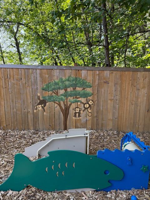 Playground with a monkey tree on a wooden fence, green fish, and blue wave-shaped structures.
