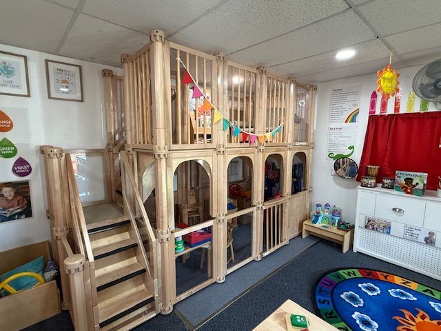 Playroom with a small loft accessible by stairs and a red slide. Includes a carpeted floor, storage, and coat rack.