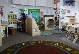 A preschool classroom with play structures, tables, and an alphabet rug.