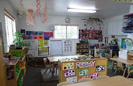Classroom interior, with art supplies, tables, chairs, and student artwork on display.