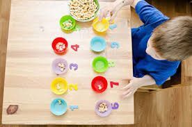 Child sorting pasta into colorful cups labeled with numbers on a wooden table.