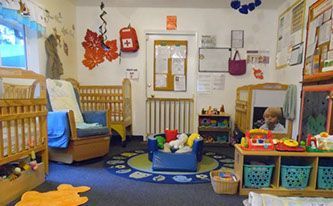 Daycare room with cribs, toys, and a child playing.