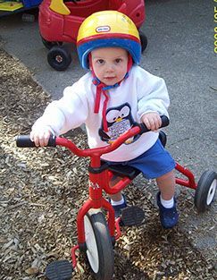 Child wearing a yellow helmet, riding a red tricycle outdoors.