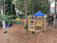 Playground with slides, swings, and climbing structures on wood chips under a blue roof.