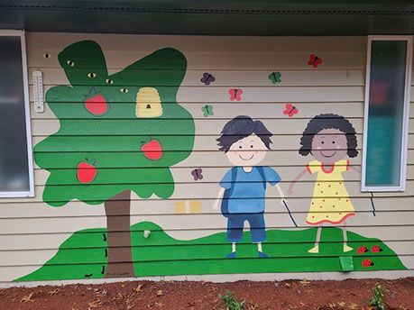 Mural of two children holding hands near an apple tree with butterflies and a grassy lawn.