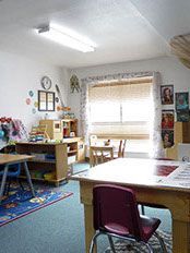 Classroom interior with tables, chairs, and children's toys and decorations.