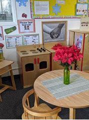 A preschool play area with a kitchen, table with flowers, and educational posters.