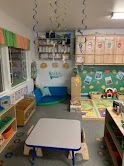 A preschool classroom with a blue couch, tables, shelves, and decorations.