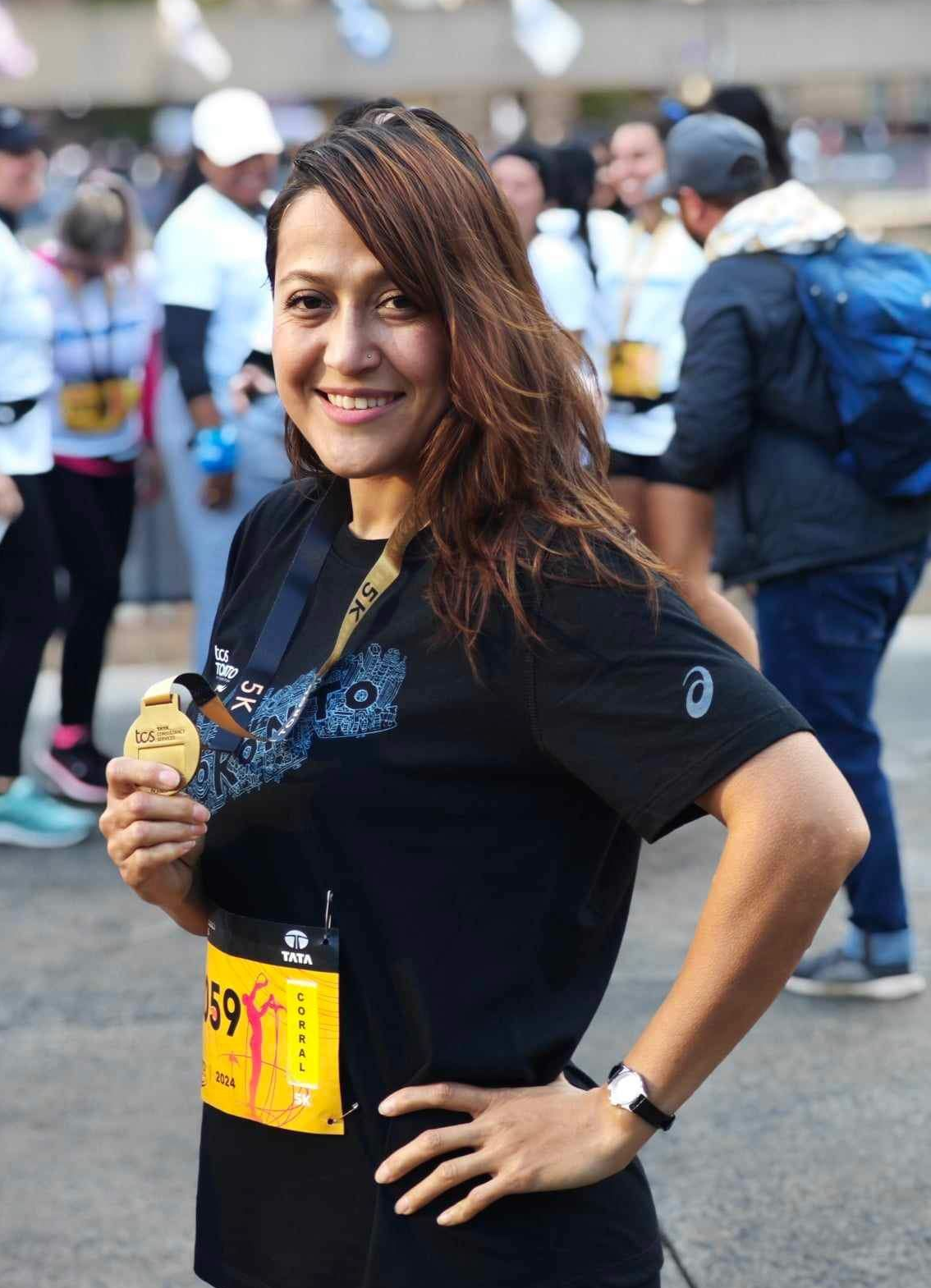 Woman in black shirt holding a medal, smiling at a race. Number 