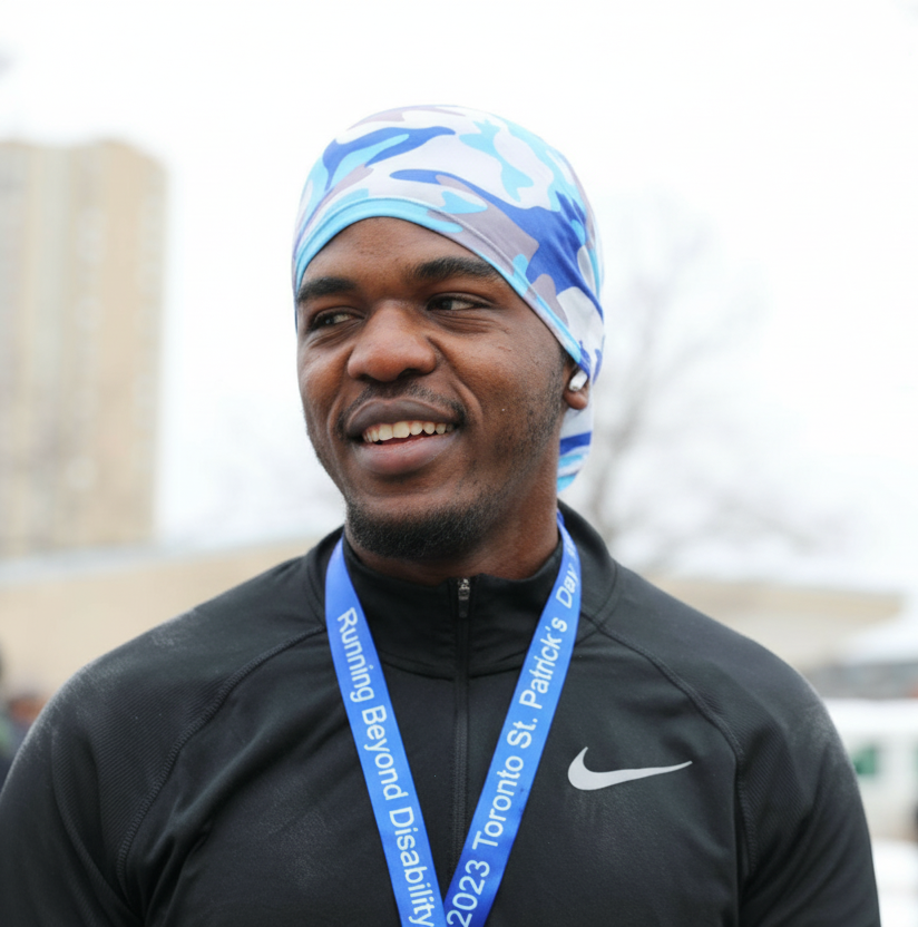Man wearing a blue camo headscarf and a medal, smiling outdoors.