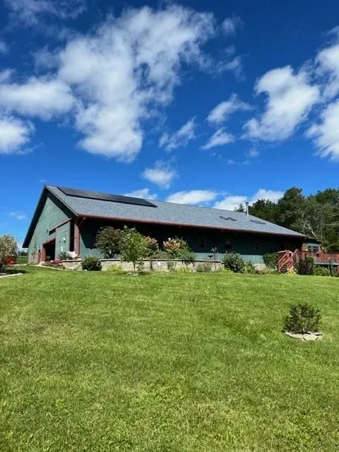 a large green barn is sitting in the middle of a lush green field