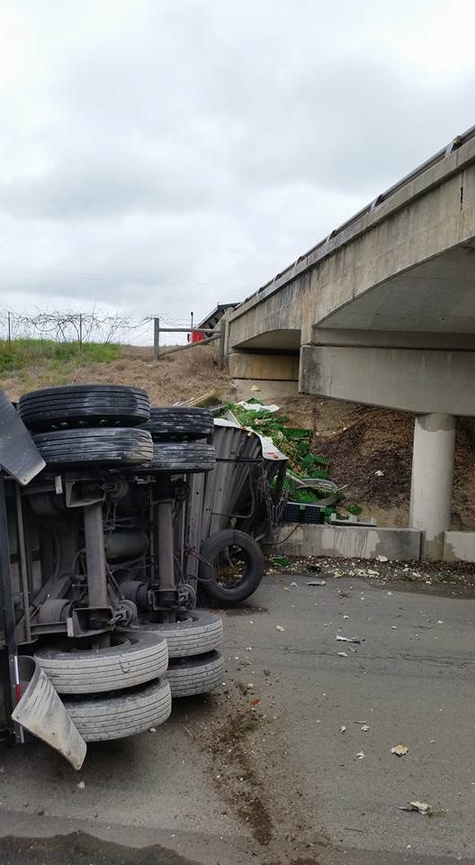 Overturned car beside highway overpass, with debris scattered on the pavement