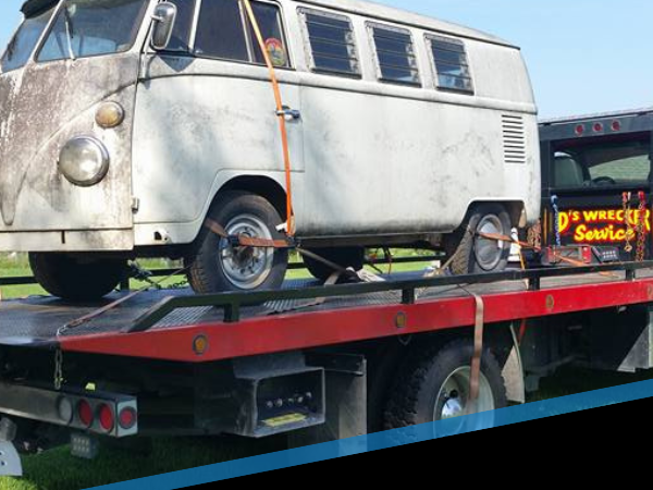 White vintage van on a flatbed tow truck, viewed from the side.