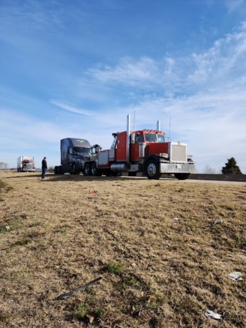 Red semi-truck and blue truck parked on a rural roadside under a clear blue sky