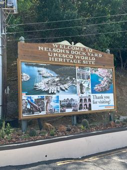 Wooden welcome sign for Nelson's Dockyard, a Heritage World site, and greenery surrounding.