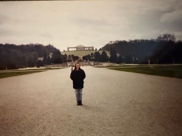 Picture of a young woman in a brown coat and blue jeans on a gravel pathway in the Schonbrun Palace Gardens