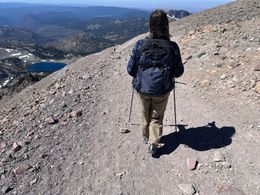 Hiker with backpack walking on a rocky mountain trail overlooking a valley