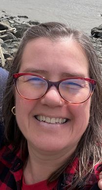 Picture of a smiling middle-aged white woman with medium-length brown hair and glasses.